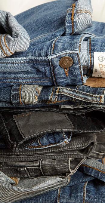 A stack of men's denim jeans in a variety of blue & black washes.