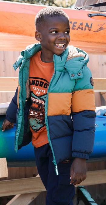 A boy wearing blue contrast colour block padded jacket and orange trim paired with brown trousers.