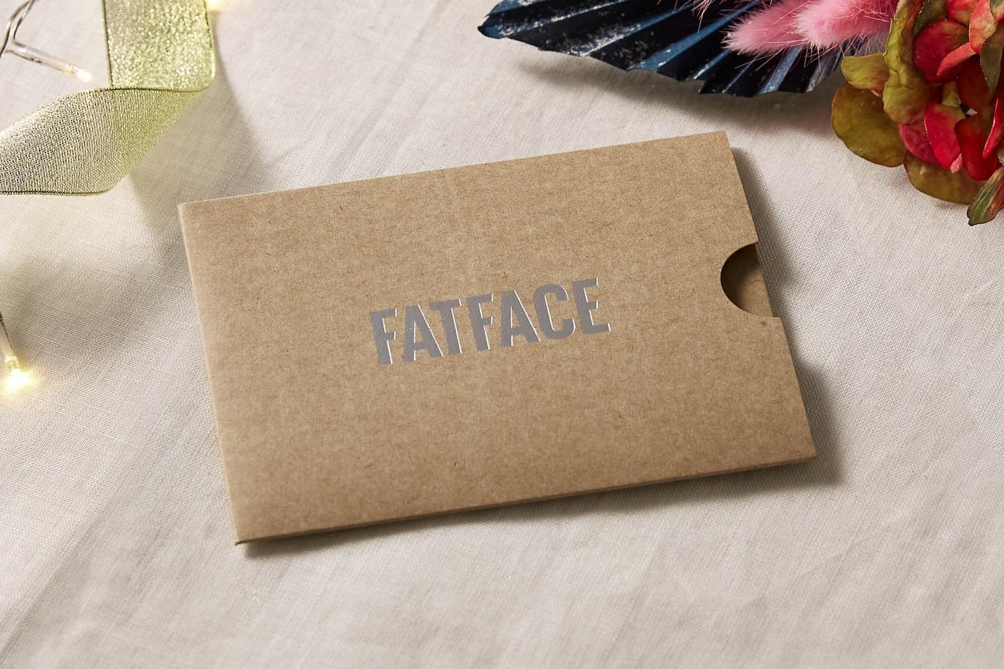 A pale brown cardboard gift card sleeve with silver foil print FatFace logo.