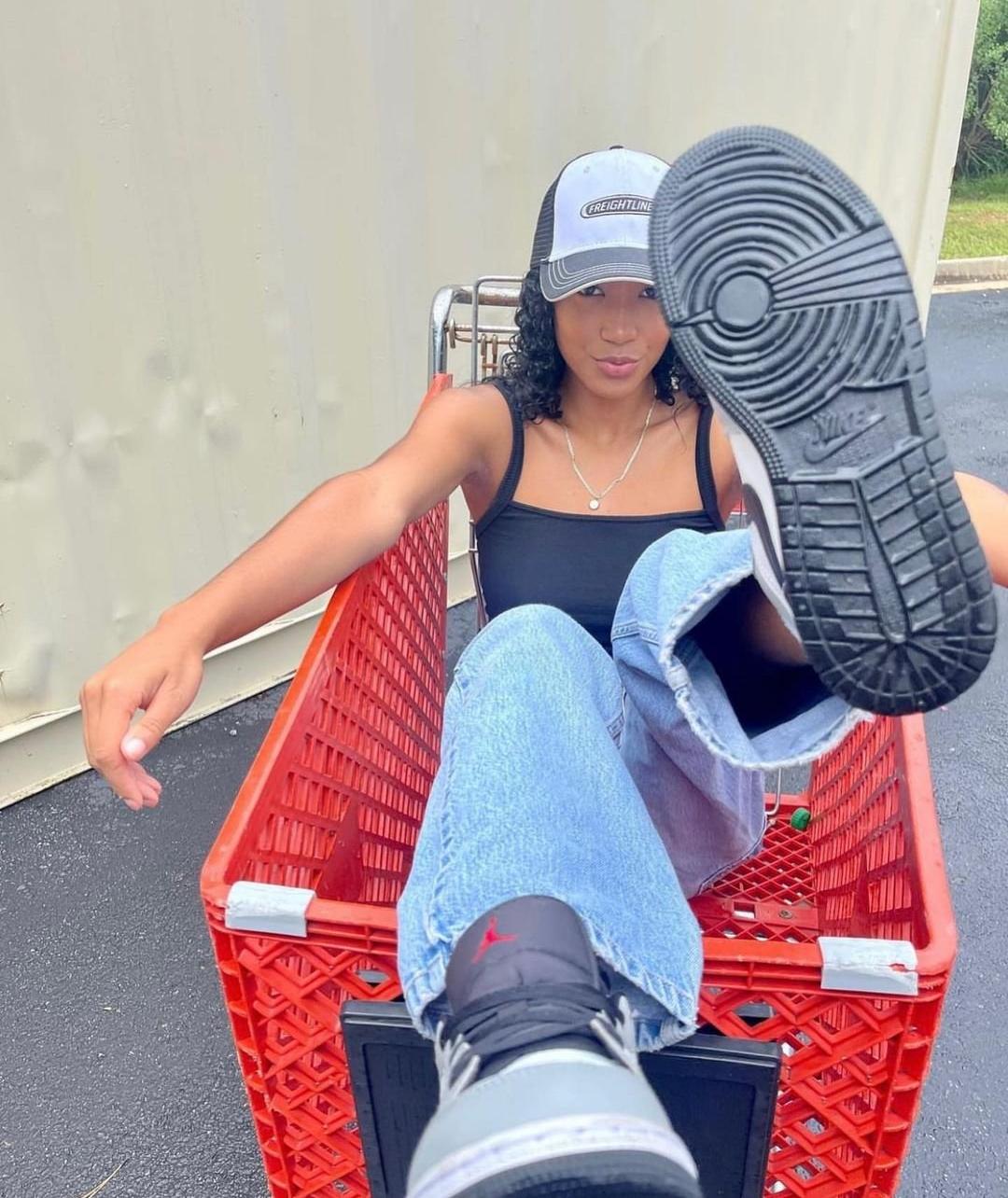Woman in jeans, black tank top, and Jordan sneakers.