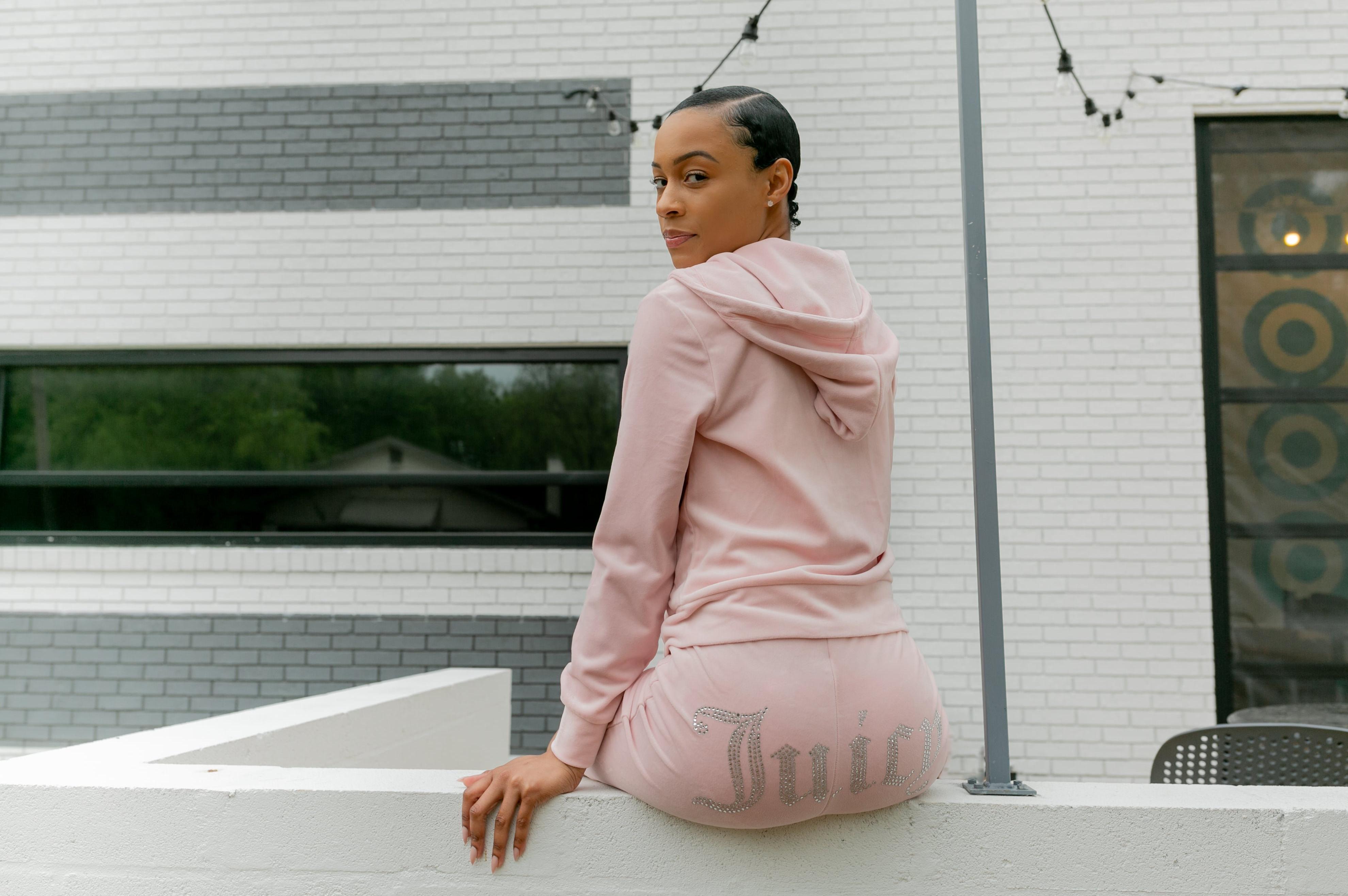 Woman sitting on ledge in pink Juicy Couture Velour jumpsuit.