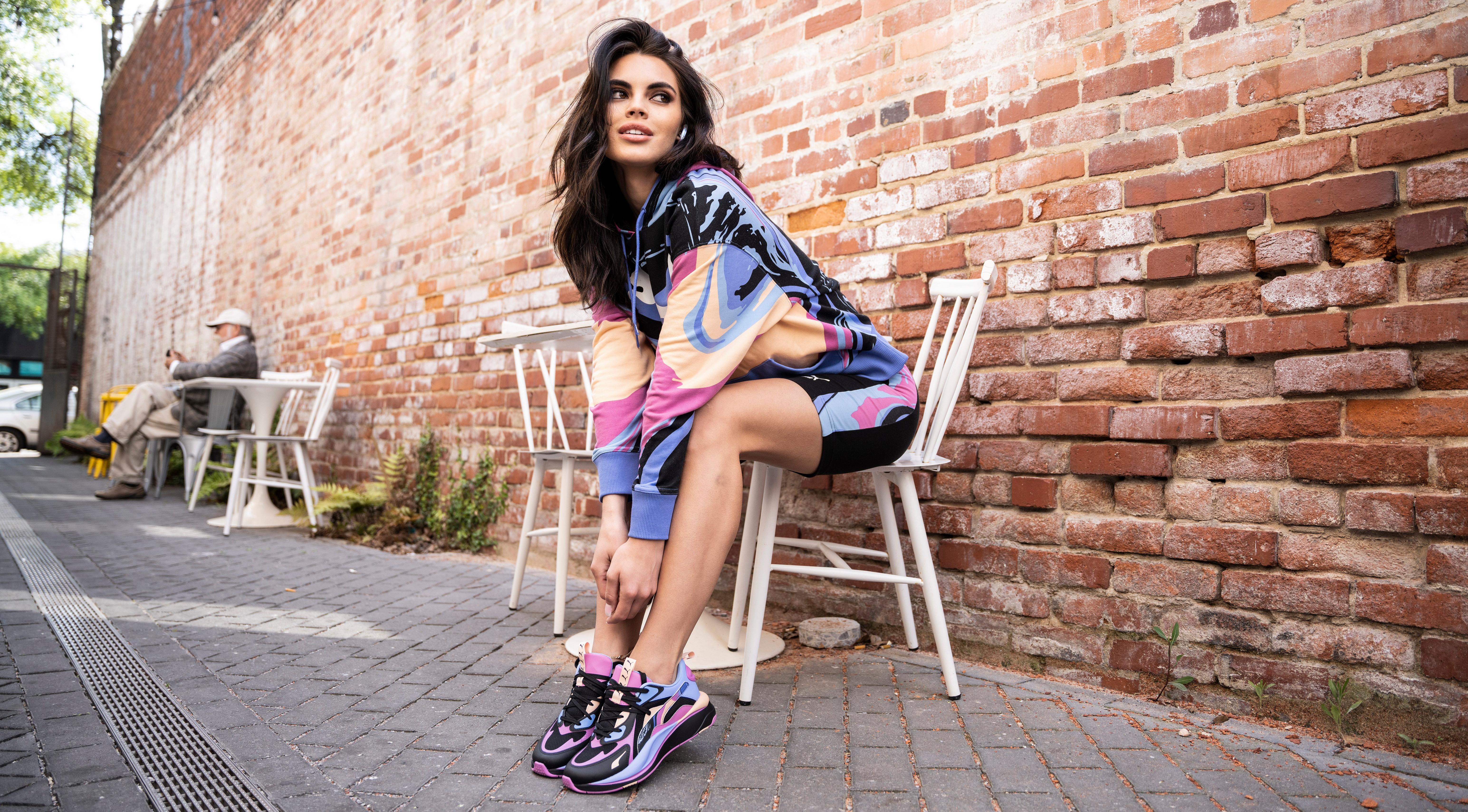 Woman posed on chair outdoors wearing Puma Marble Pack apparel and footwear, exclusively at Hibbett | City Gear.
