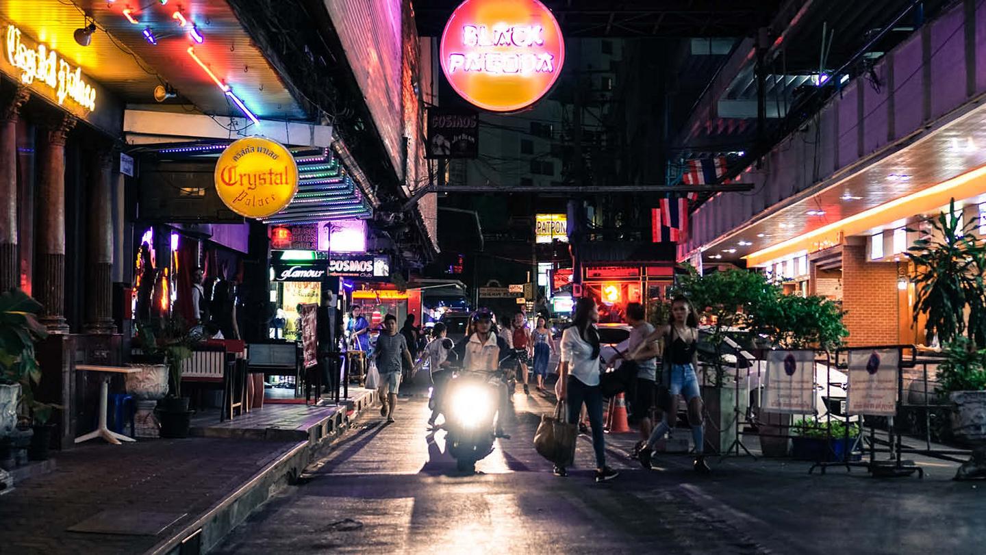 A busy street scene at night in Bangkok, with bright neon lights and lots of people