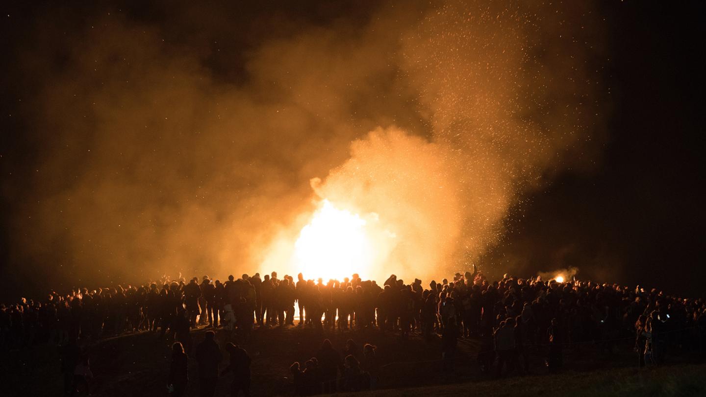 A huge group of spectators watching a spectacular bonfire at night time 