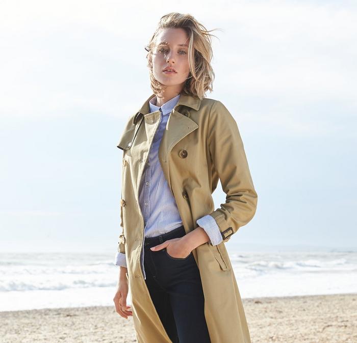 Woman wearing the FatFace trench coat whilst walking on the beach