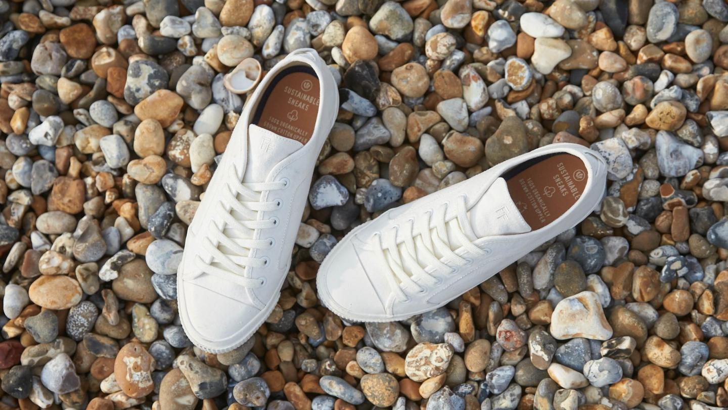 White lace up trainers on a pebbly beach