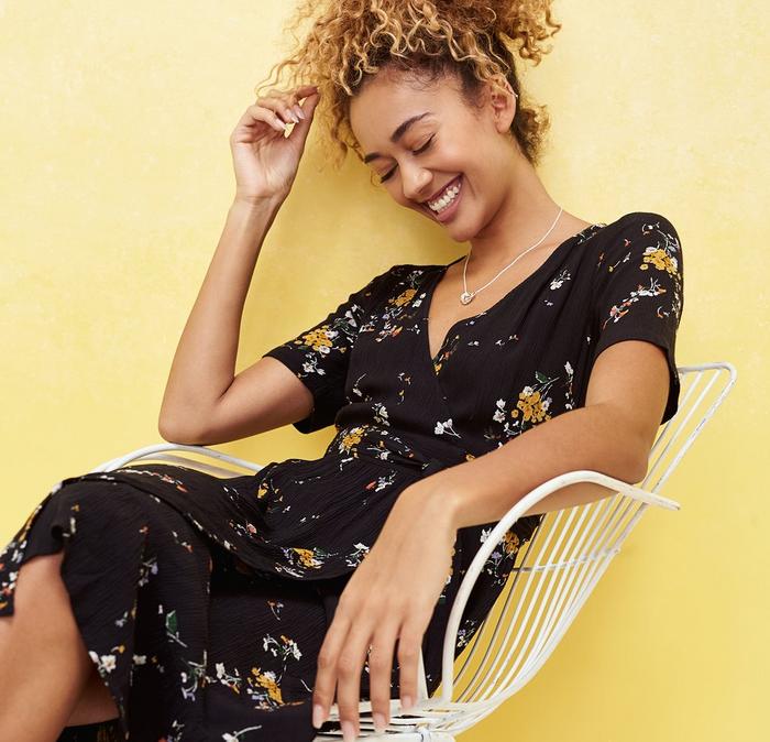 A curly haired model wear a black FatFace wrap dress with yellow pops of print