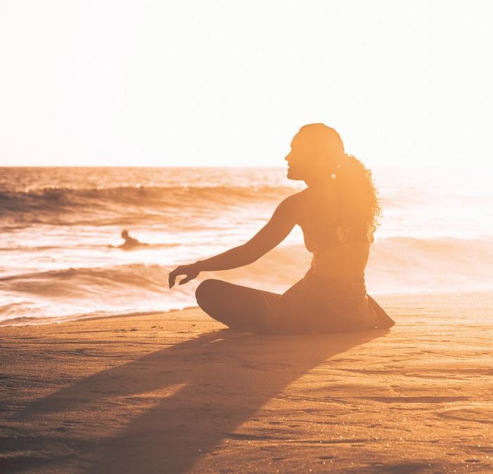 A young woman sitting on a sandy beach at sunset
