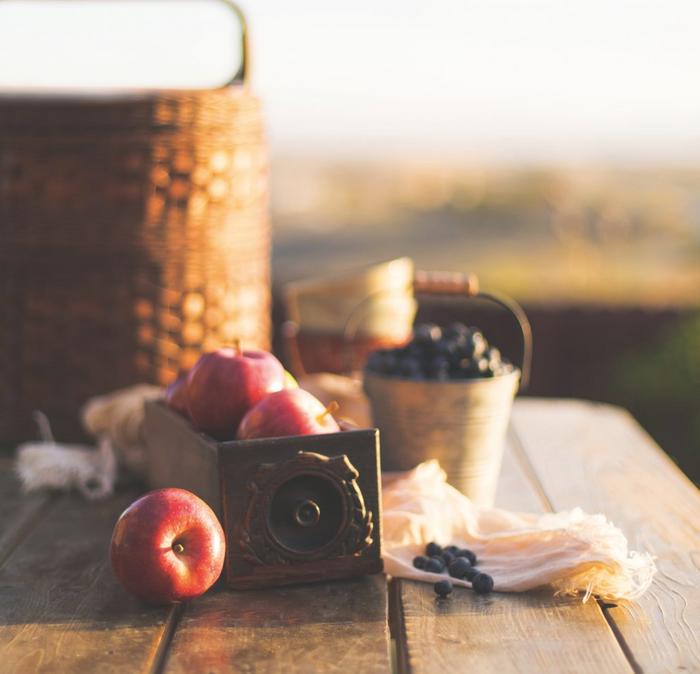 Fruit and a picnic hamper set up on a picnic table in the countryside at sunset