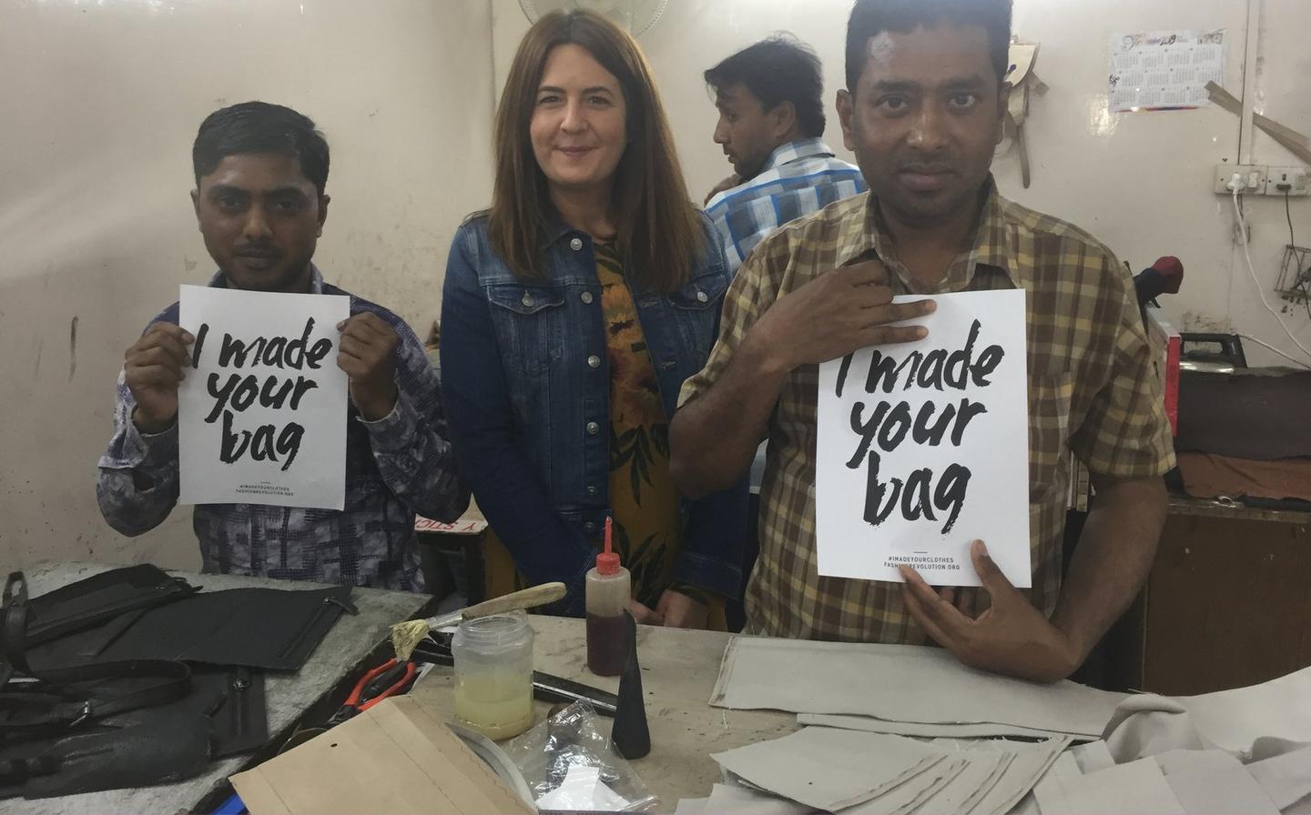 A group of people all holding, I made your bag, signs in a factory.