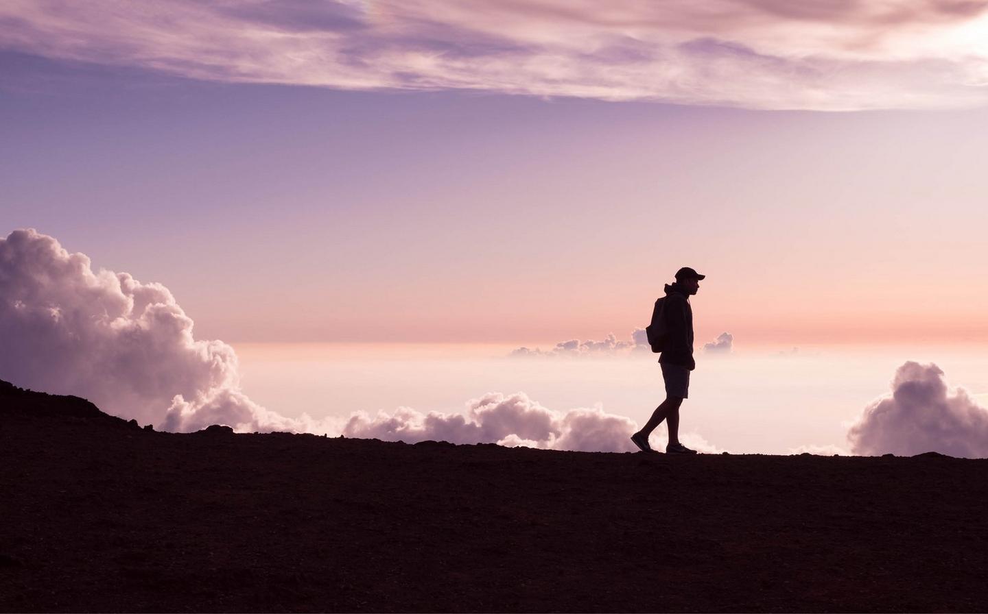 A silhouetted person going on a stroll with a backdrop of a beautiful purple sunset and fluffy clouds
