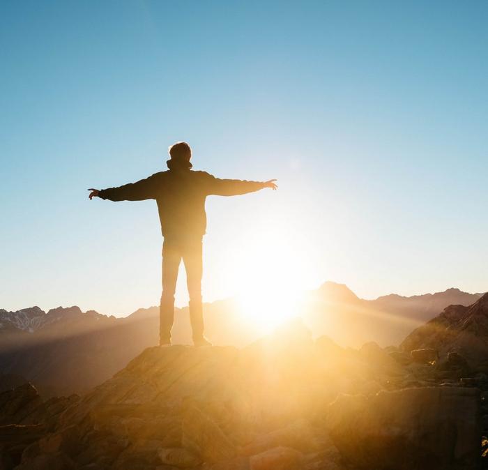 A hiker standing on a mountaintop with his arms outstretched during sunrise