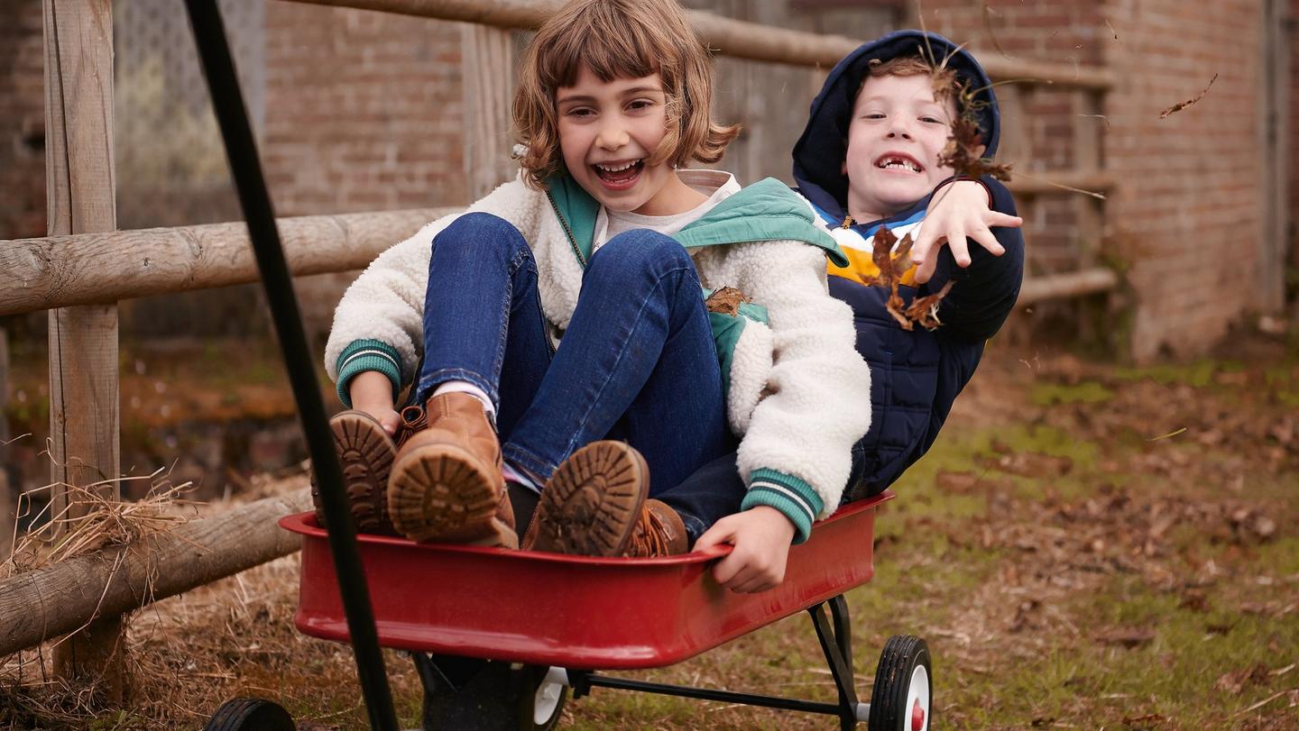 Two kids bundled up in autumn clothes playing on a makeshift go-kart.
