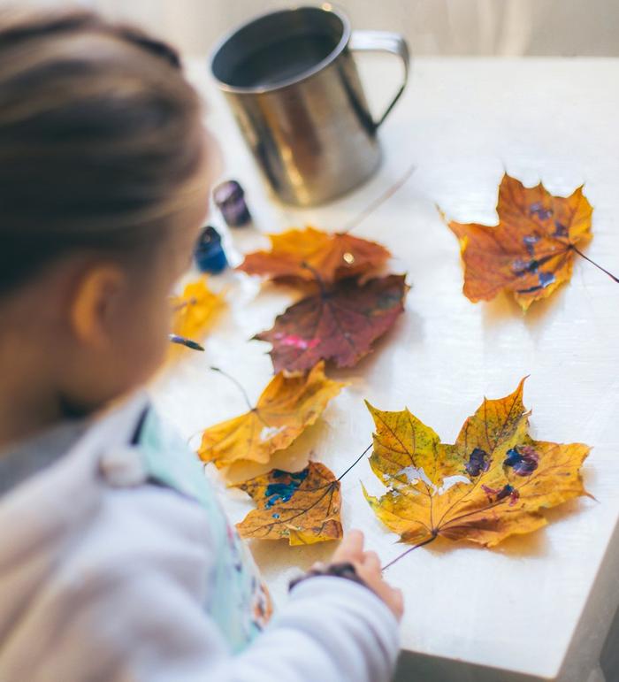 A little girl painting golden leaves laid out on a table.