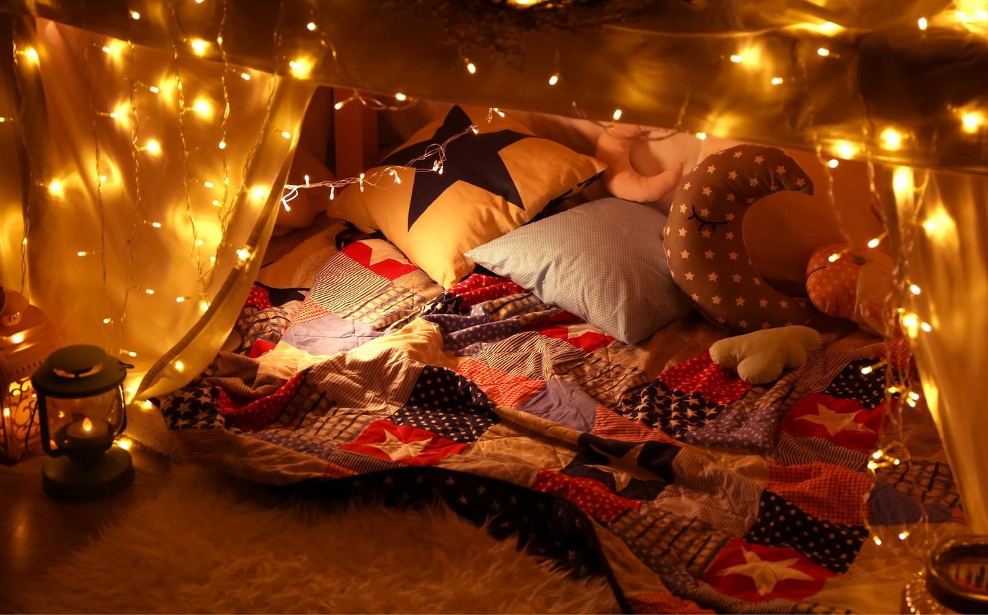 An indoor fort filled with blankets cushions and fairy lights