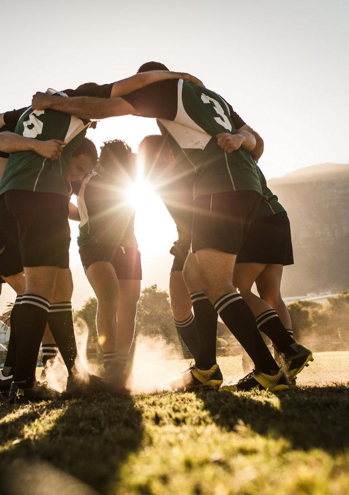 A group of rugby players in a green kit, stood in a circle during a team pep talk.