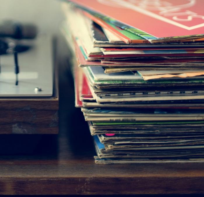 A stack of old vinyl records next to a record player on a table.