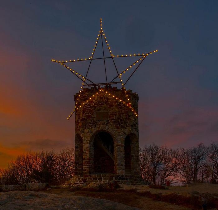 A large metal star decorated in lights on top of a stone tower on Mount Battie, Maine.