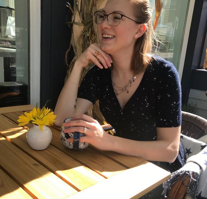 Women sat at a table outside clutching a mug of coffee wearing glasses and a navy dress
