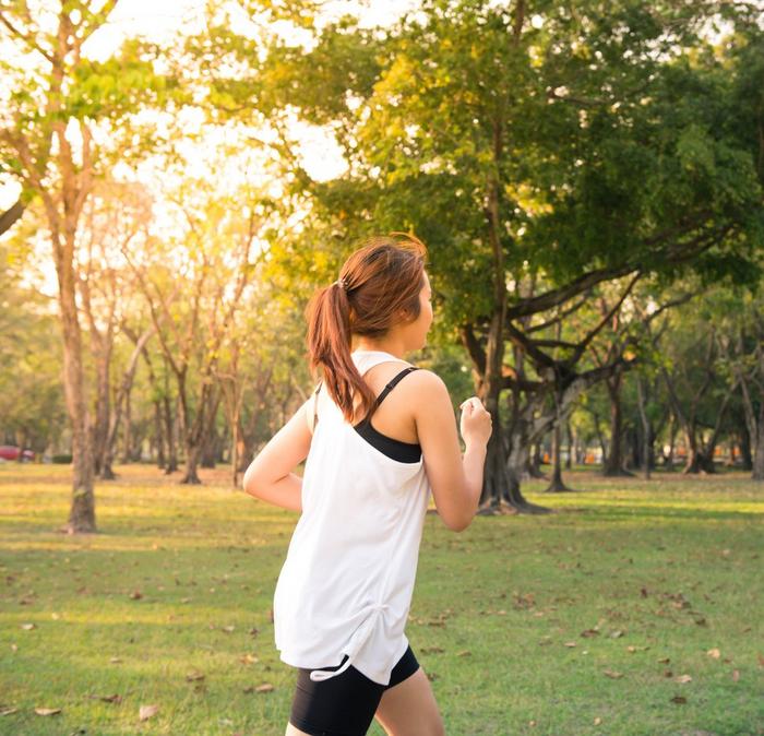 A woman wearing a white vest & black shorts running in a park.