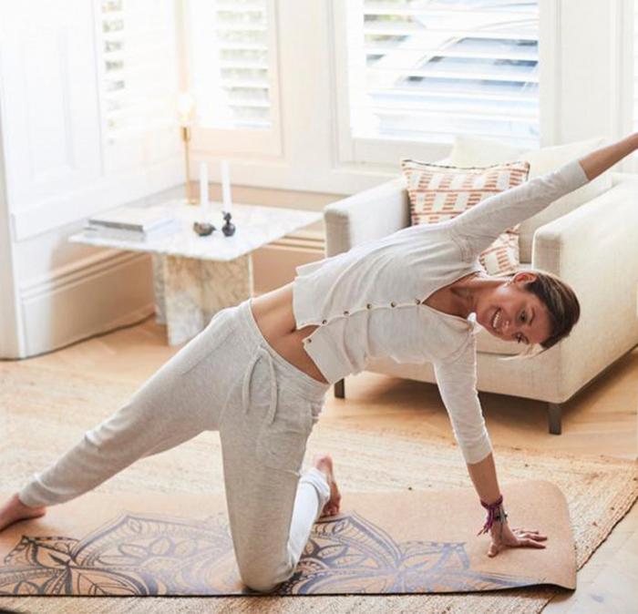 A woman wearing a white button-up top and grey jogging bottoms doing yoga in her living room.