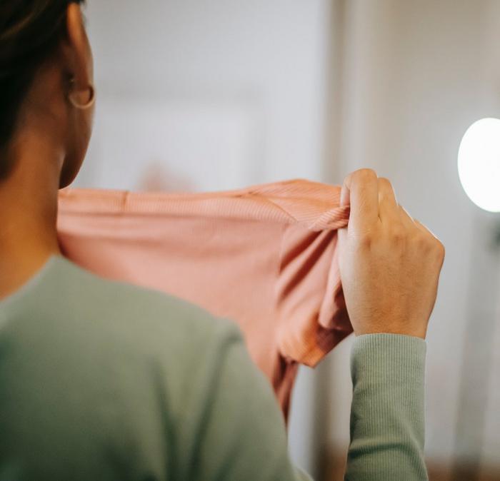 A woman holding out a textured salmon pink T-shirt.