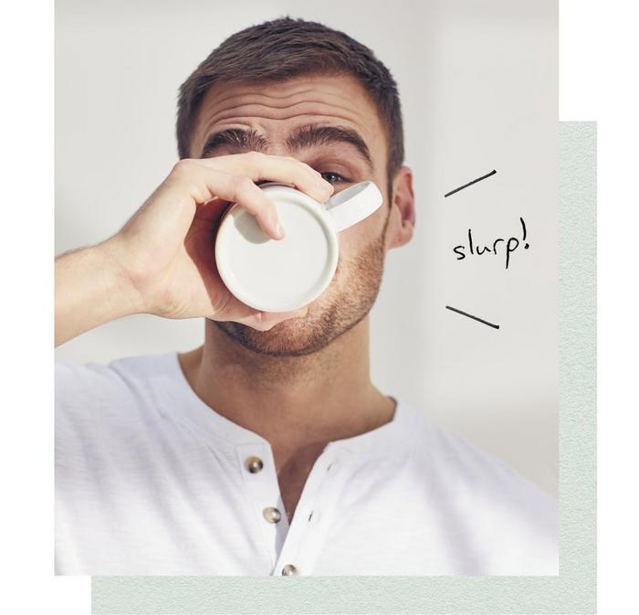 A man drinking from a white mug.