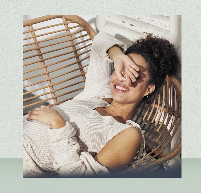 A woman relaxing in a wicker chair on a porch, shielding her eyes from the sun.
