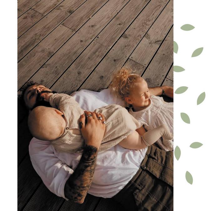 A family photo featuring Tom lying on wooden decking with his two young children.