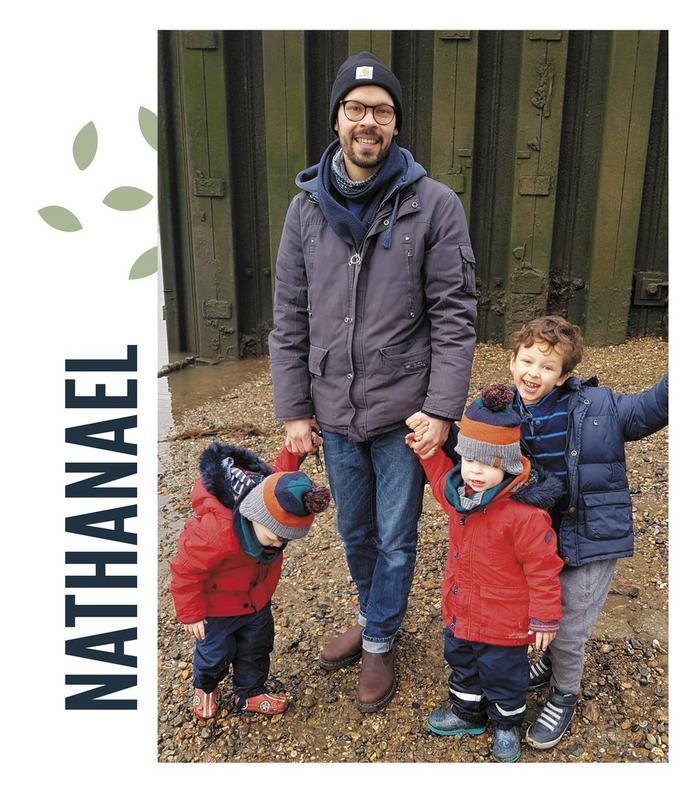 A family photo featuring dad Nathanael holding the hands of his three young sons, on a family walk.