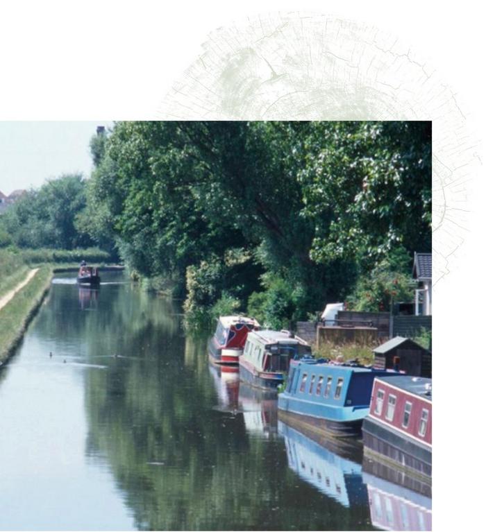 A countryside canal with boats moored up along the edge.