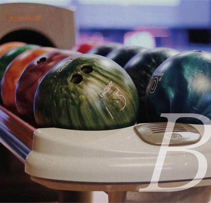 A rack of different coloured bowling balls at a bowling alley.