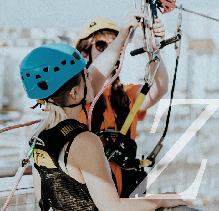 Two women in helmets & harnesses, preparing to zip line.