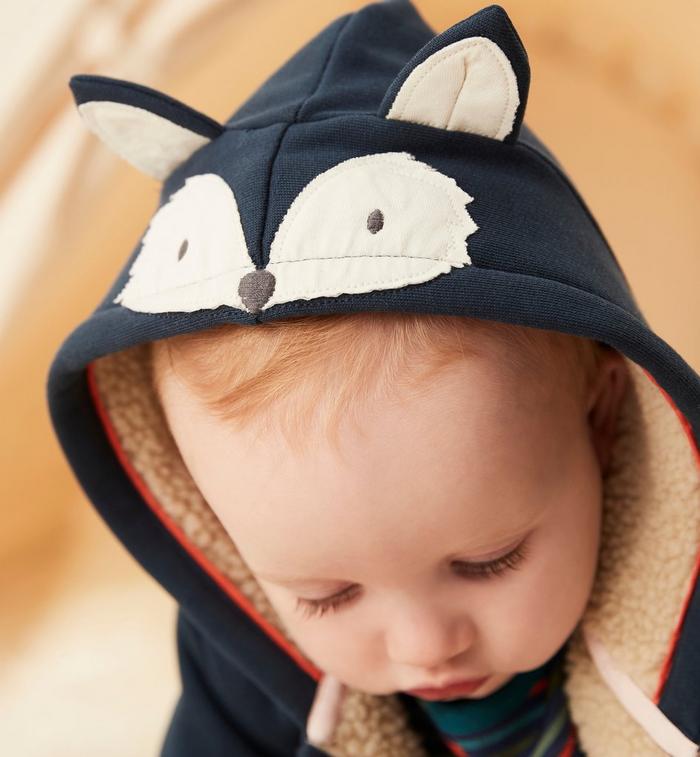 A baby boy wearing a soft borg-lined navy hoodie with a cute animal face and ears design on the hood.