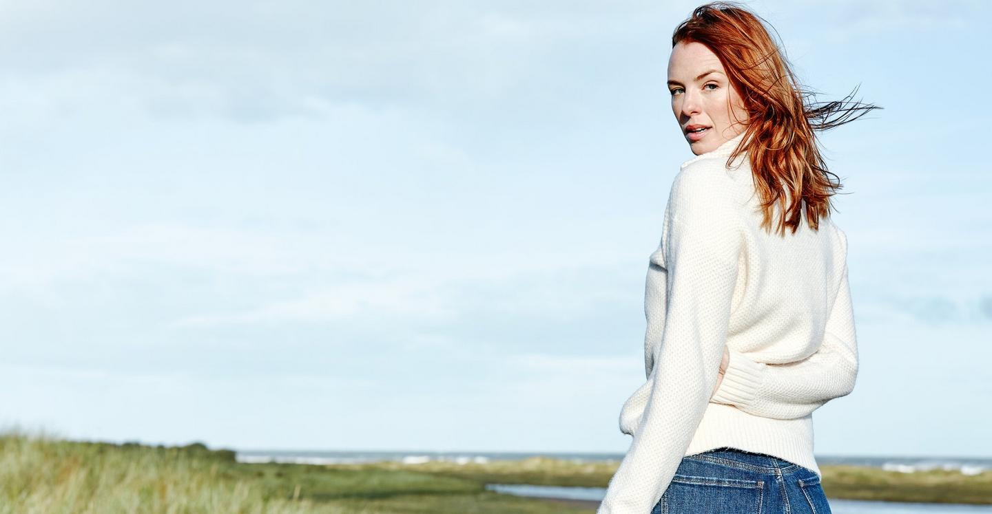 A woman wearing a textured knit ivory jumper with half zip neck, & blue jeans.