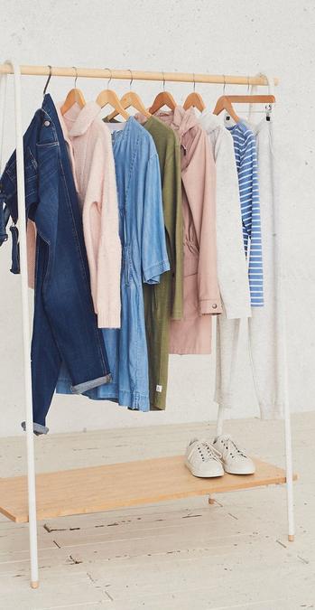 A selection of women's clothes, including dungarees, tops & coats, hanging on a rail.