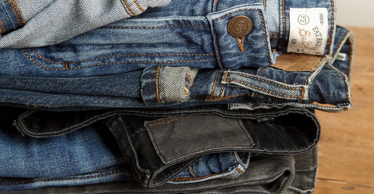 Close up on a stack of men's denim jeans in various blue & black washes.