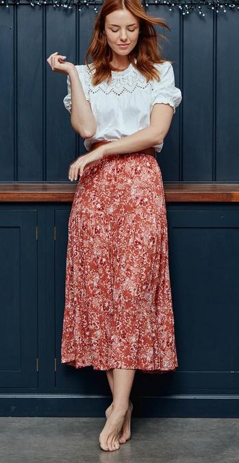 Woman wearing a short-sleeved white broderie blouse & a tiered midi skirt with ditsy floral print in red & pink hues.