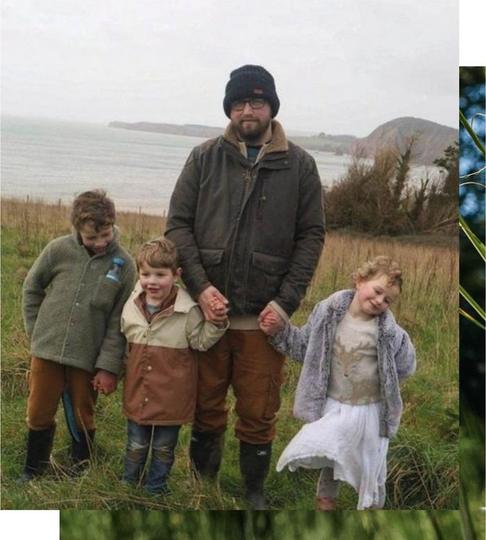 A father and his three small children pause for a photo in a field overlooking a bay.
