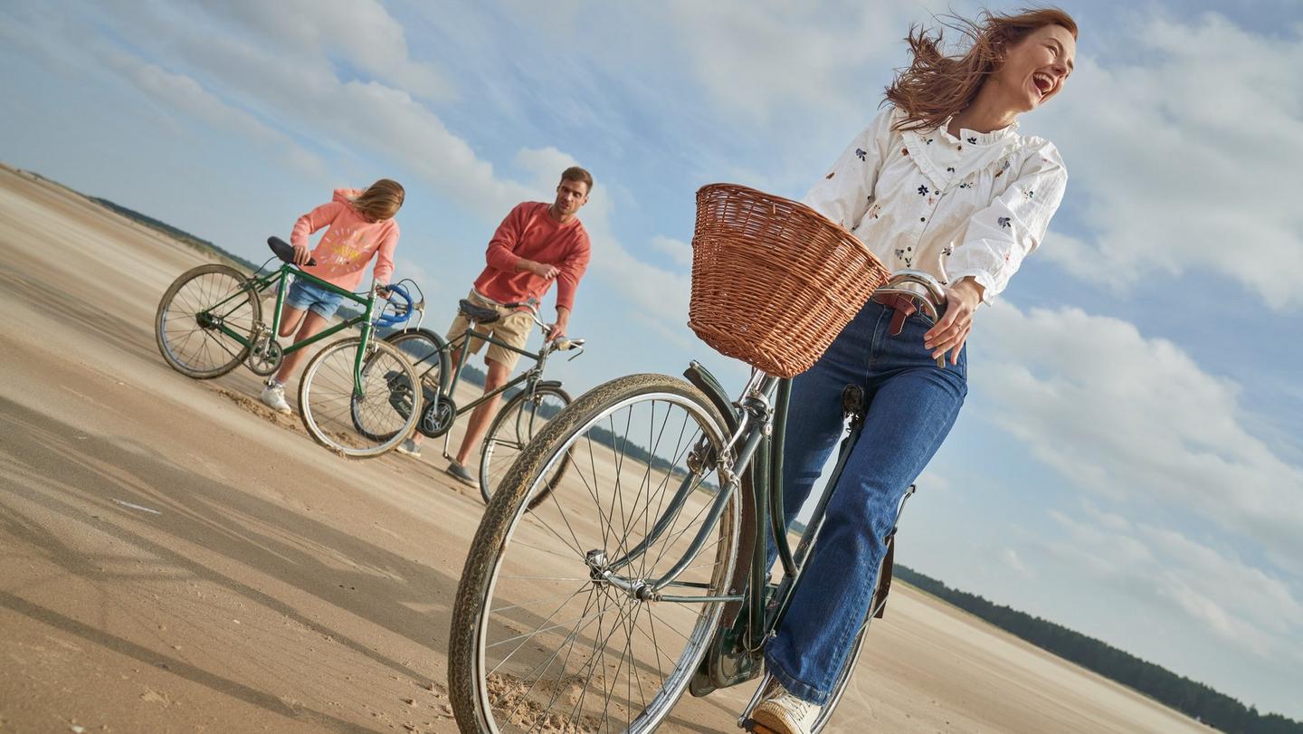 A family of three riding old-fashioned bicycles on a sandy beach.