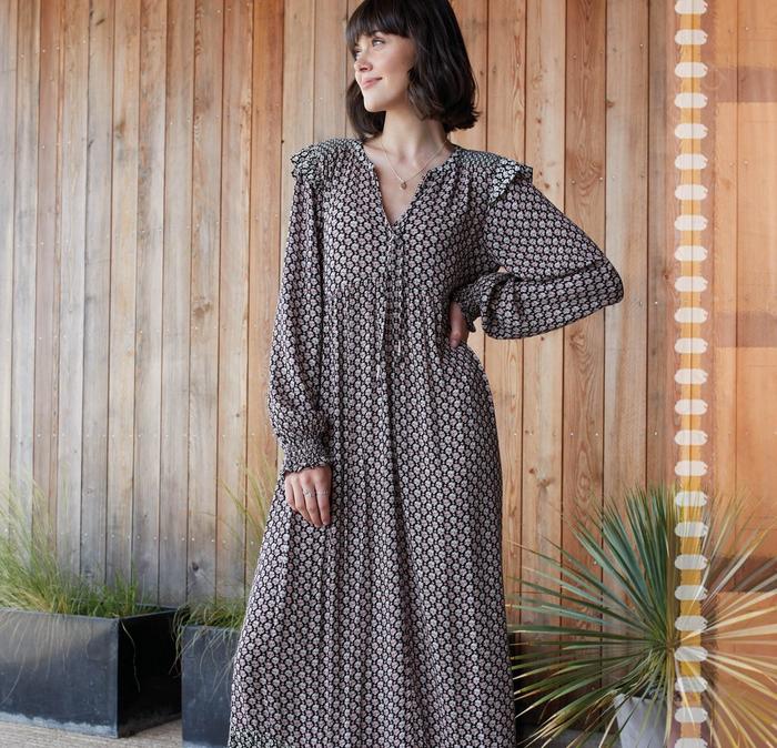 A woman wearing a long-sleeved V-neck maxi dress with ruffle shoulders & floral tile print.