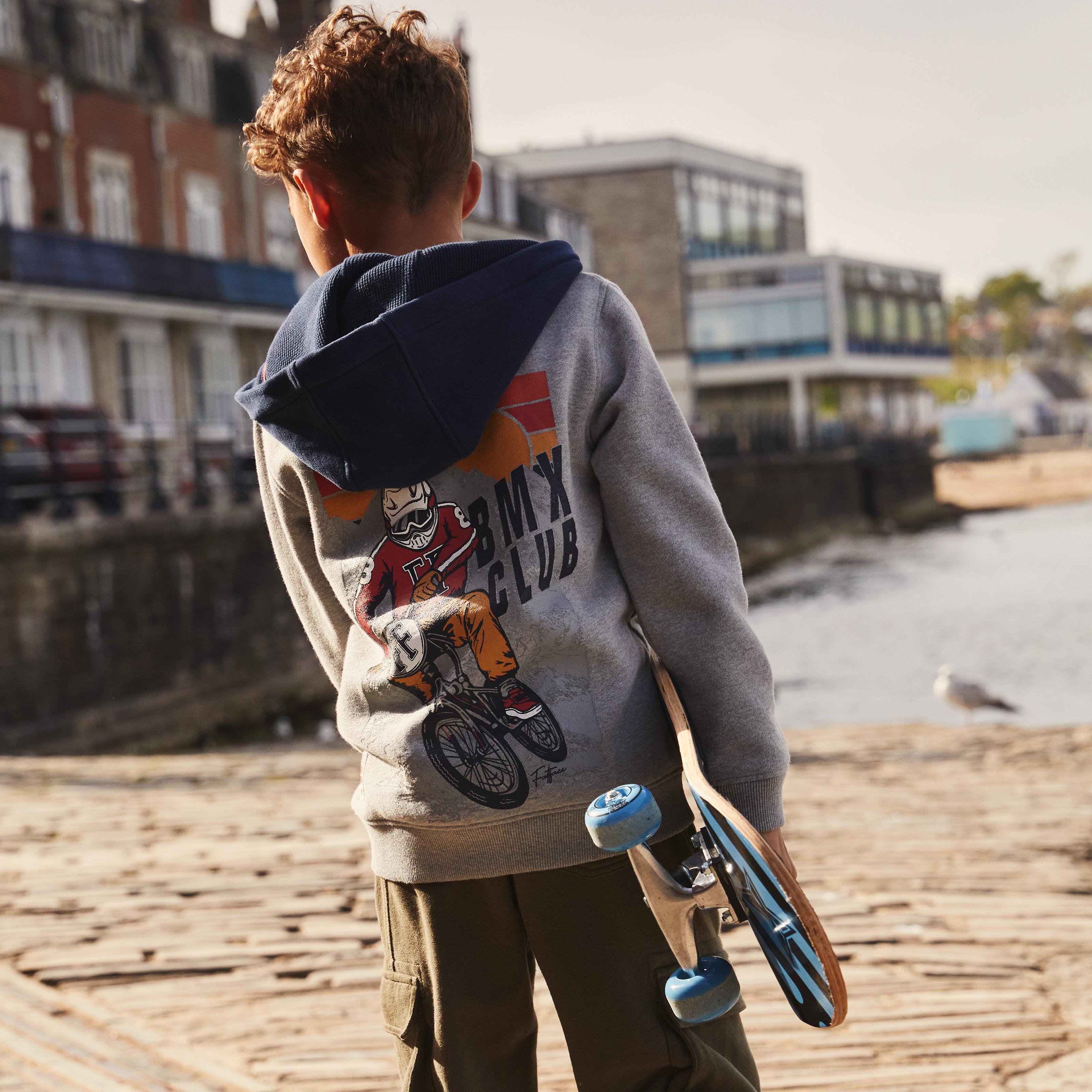 Boy wearing a grey hoodie with navy blue hood & 'BMX Club' graphic on the back, paired with green jersey cargo trousers.