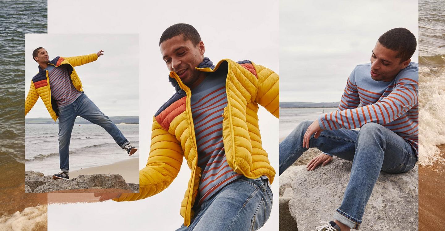 Man wearing a yellow padded jacket with navy & orange colour block stripes, over a blue & red striped T-shirt & blue jeans.
