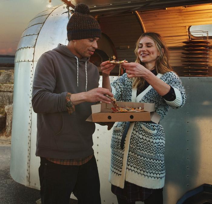 A man & a woman dressed in warm layers enjoy a pizza from a street food van.