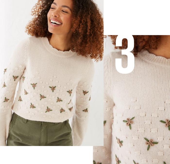 A woman wearing an ivory sweater with bobble texture & embroidered flowers, & green pants.
