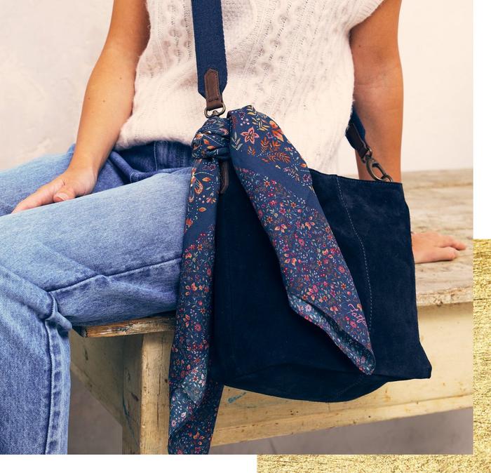 A blue fabric wrap with multicolored floral print tied around the strap of a blue suede bag.