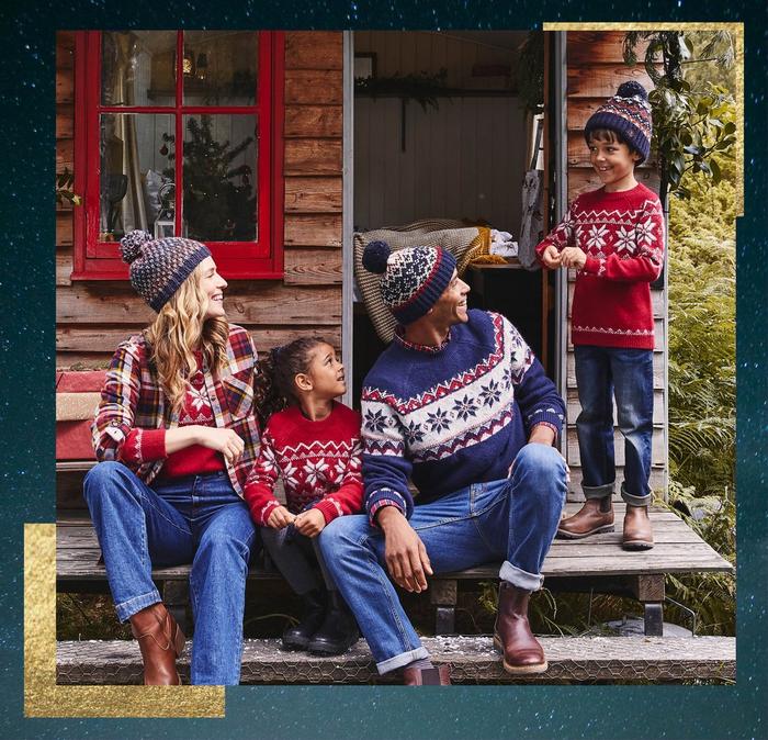 A family sitting on the porch of a wood cabin, wearing brightly colored Fair Isle knit sweaters.