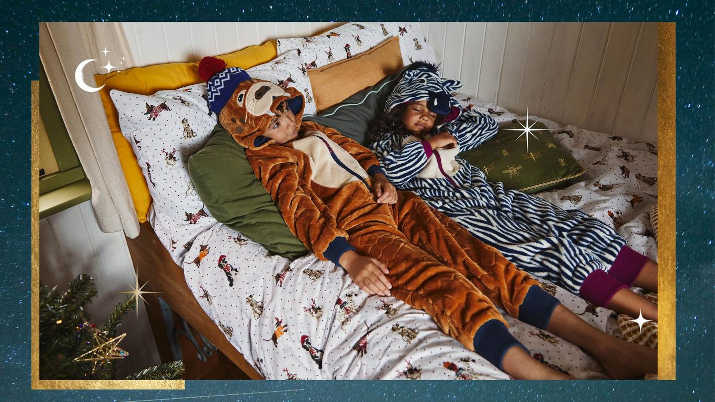 A boy wearing a Walrus character onesie with navy cuffs, & a girl wearing a Zebra character onesie with pink cuffs.