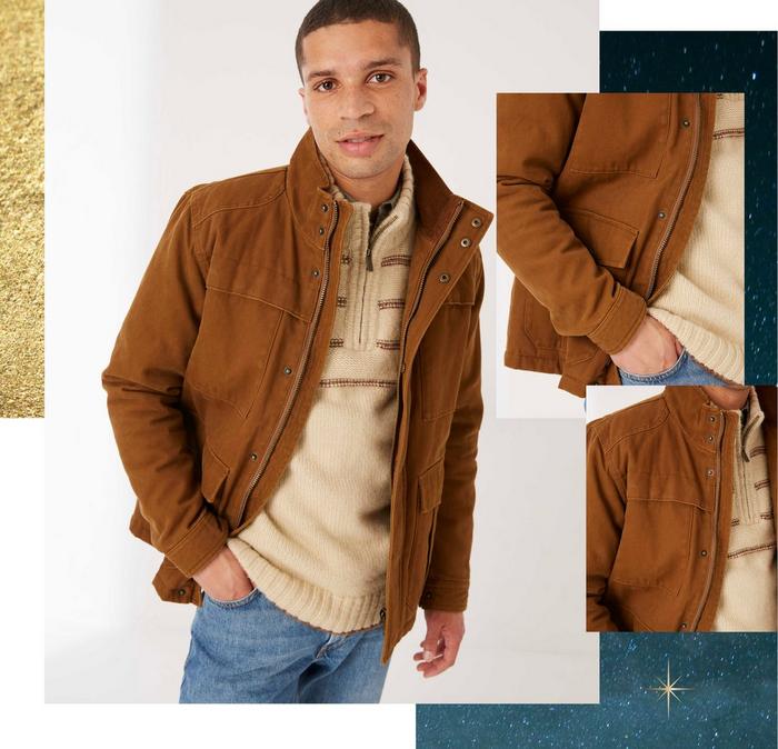 A man wearing a tan brown canvas jacket over a zip half-neck sweater & blue jeans.