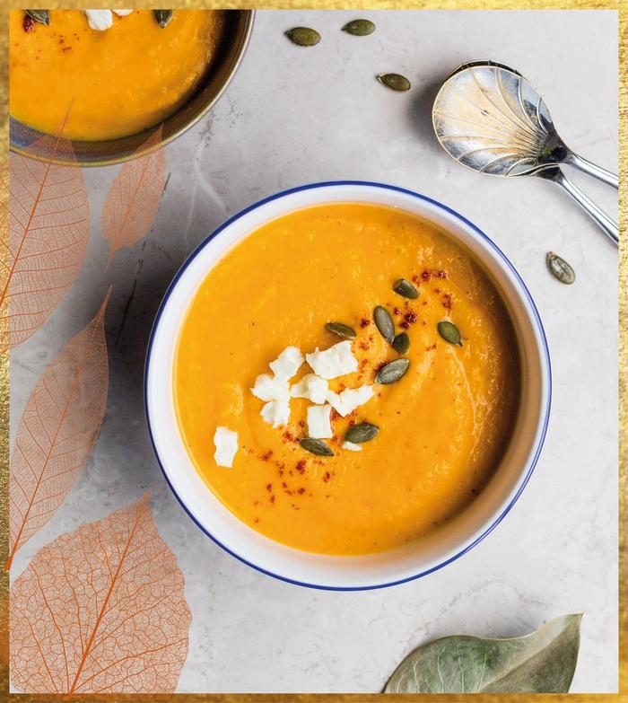 Two bowls of bright orange butternut squash soup topped with crumbled cheese and seeds.